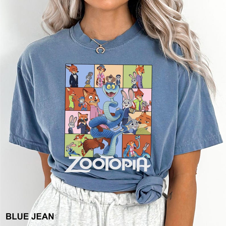 May include: Blue jean colored t-shirt featuring a colorful graphic of characters from the animated movie Zootopia. The graphic includes the movie title and various character illustrations. The shirt is made of a soft material.