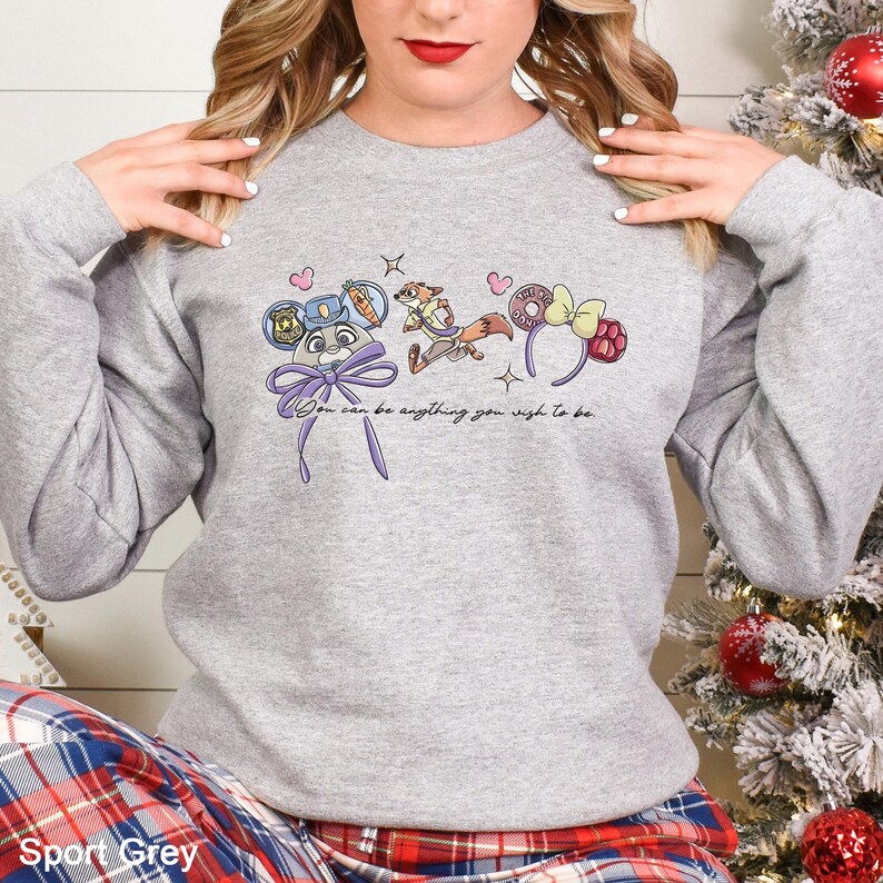 May include: A Sport Grey sweatshirt with a playful design featuring cartoon characters and the text "You can be anything you wish to be." The design includes a mouse-eared hat, a fox, and a bow. The sweatshirt is a comfortable, casual style.