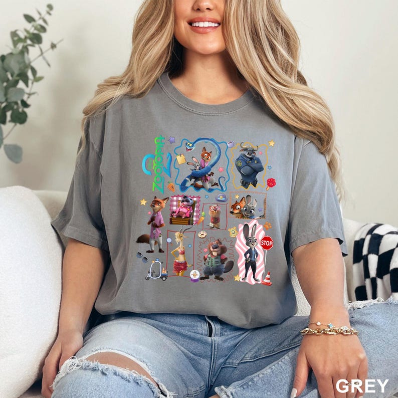 May include: A grey short-sleeve t-shirt featuring a Zootopia graphic print. The design includes various characters from the film, such as Judy Hopps and Nick Wilde, arranged in a collage with small icons like a stop sign, a scooter, and a donut.
