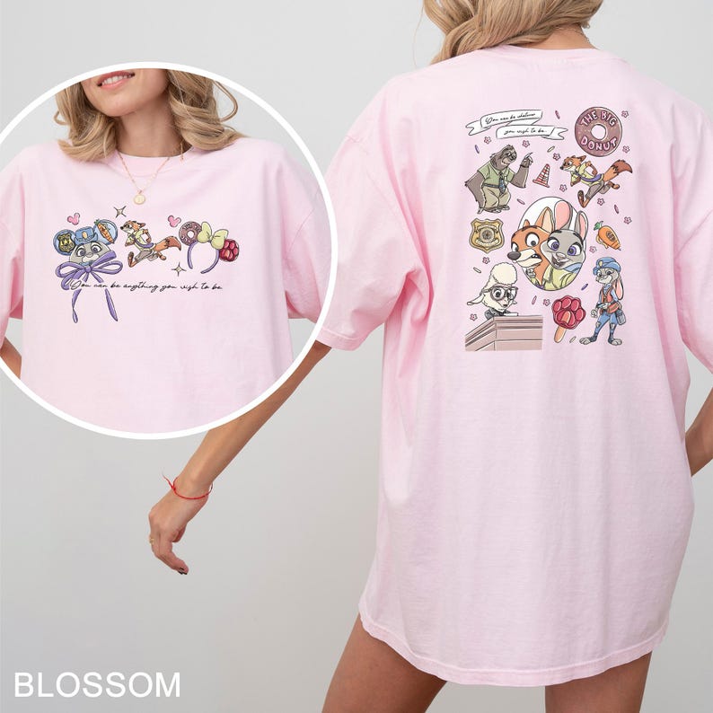 May include: Pale pink t-shirt with cartoon characters and the text "You can be anything you wish to be." The back of the shirt has a graphic of cartoon characters and the text "The Big Donut."