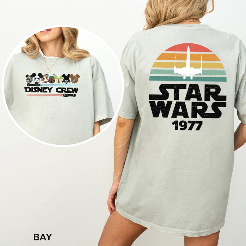 May include: Pale green t-shirt with a Disney Crew graphic on the front and a Star Wars design on the back. The front graphic shows Mickey Mouse, Minnie Mouse, and other Disney characters. The back graphic features a sunset design with the text "STAR WARS 1977".
