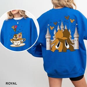 May include: Royal blue sweatshirt featuring a graphic of two chipmunks in a teacup with balloons. The back of the sweatshirt has a graphic of two chipmunks hugging in front of a castle with Mickey Mouse balloons. The word "ROYAL" is printed at the bottom.