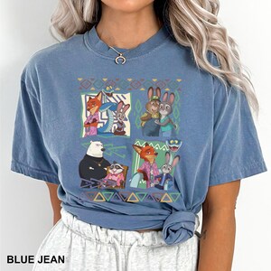 K&ouml;nnte beinhalten: Blaues Jeans-T-Shirt mit einem farbenfrohen Grafikdesign von Zeichentrickfiguren. Die Grafik zeigt Bilder eines Fuchses, einer Schlange, eines Kaninchens, eines B&auml;ren und eines Waschb&auml;ren. Das Shirt hat einen Rundhalsausschnitt und kurze &Auml;rmel.
