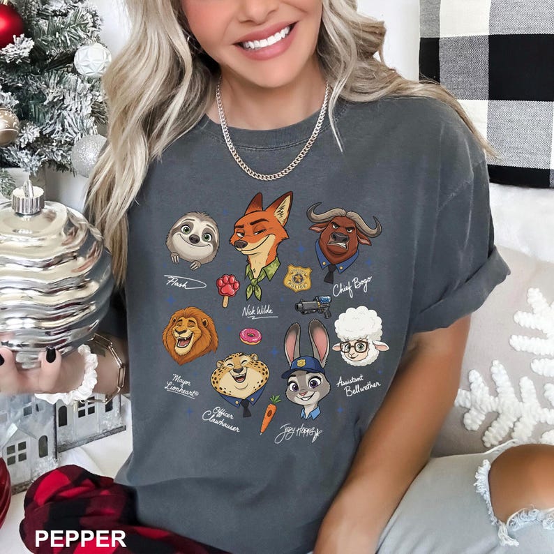 K&ouml;nnte beinhalten: Dunkelgraues T-Shirt mit Zeichentrickfiguren aus Zootopia, darunter Flash, Nick Wilde und Judy Hopps. Das Shirt hat einen Rundhalsausschnitt und kurze &Auml;rmel. Das Wort "PEPPER" steht unten.