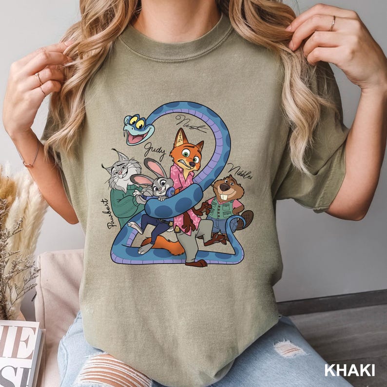 Peut inclure: T-shirt kaki avec un dessin anim&eacute; de personnages de Zootopie. Le motif comprend un serpent bleu enroul&eacute; autour du chiffre 2, avec les noms des personnages &eacute;crits au-dessus. Le mot "KHAKI" est imprim&eacute; en bas.