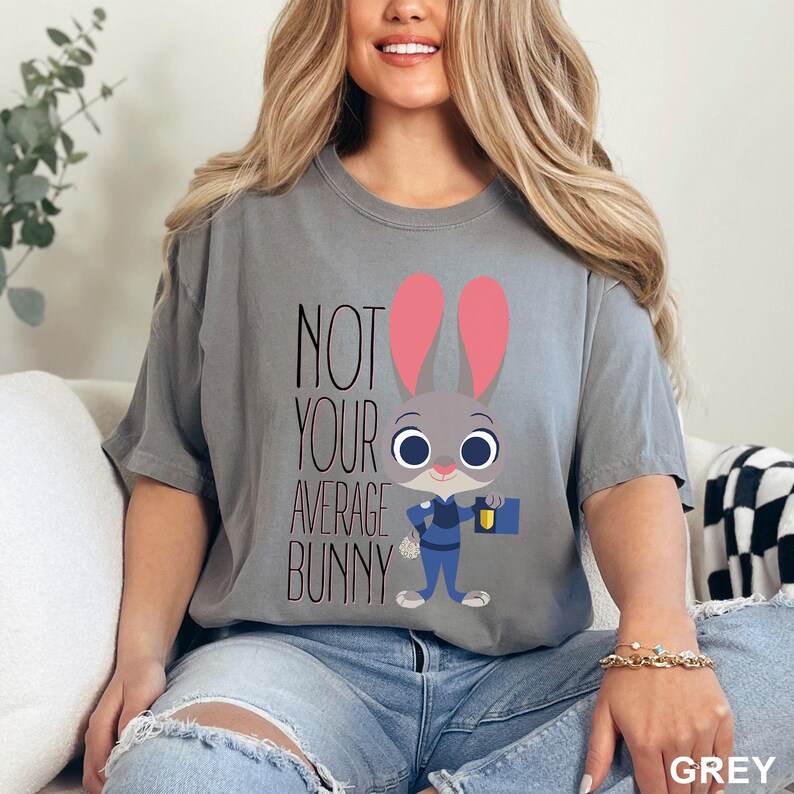 May include: Grey t-shirt with the text "NOT YOUR AVERAGE BUNNY" and a cartoon bunny character wearing a police uniform. The bunny has pink ears and is holding a briefcase and a flashlight.