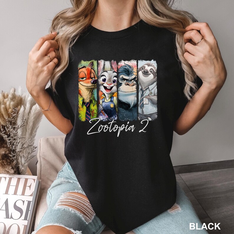 Peut inclure: T-shirt noir avec un graphisme color&eacute; des personnages de "Zootopie 2". Le design comprend Nick Wilde, Judy Hopps, le chef Bogo et Flash. Les mots "Zootopia 2" sont &eacute;crits en blanc.
