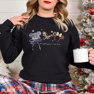 May include: Black sweatshirt with a colourful graphic featuring cartoon characters and the text "You can be anything you wish to be." The sweatshirt has long sleeves and a crew neck.