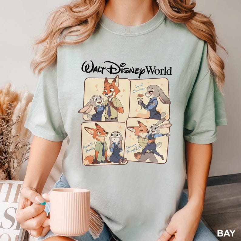 K&ouml;nnte beinhalten: Hellgr&uuml;nes T-Shirt mit einem Cartoon-Design mit Charakteren aus Zootopia. Das Design zeigt Nick Wilde und Judy Hopps in vier Panels. Der Text "Walt Disney World" ist oben auf dem Shirt aufgedruckt.