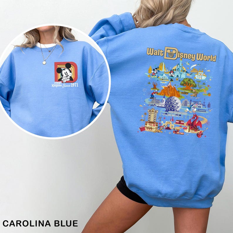 May include: Carolina blue sweatshirt featuring Mickey Mouse and the text "Magic Kingdom Since 1971" on the front. The back displays a colorful graphic of Walt Disney World with various park attractions. A comfortable, casual top.