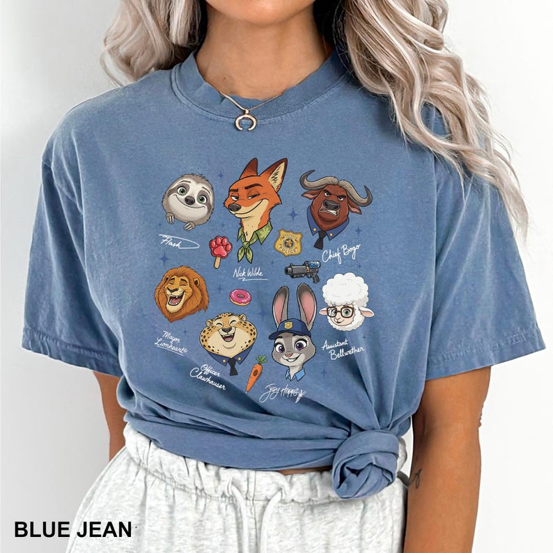 K&ouml;nnte beinhalten: Ein blaues Jeans-T-Shirt mit einer farbenfrohen Grafik von Charakteren aus dem Animationsfilm Zootopia. Die Grafik zeigt Flash, Nick Wilde, Judy Hopps und Chief Bogo. Der Text "BLUE JEAN" ist unten aufgedruckt.