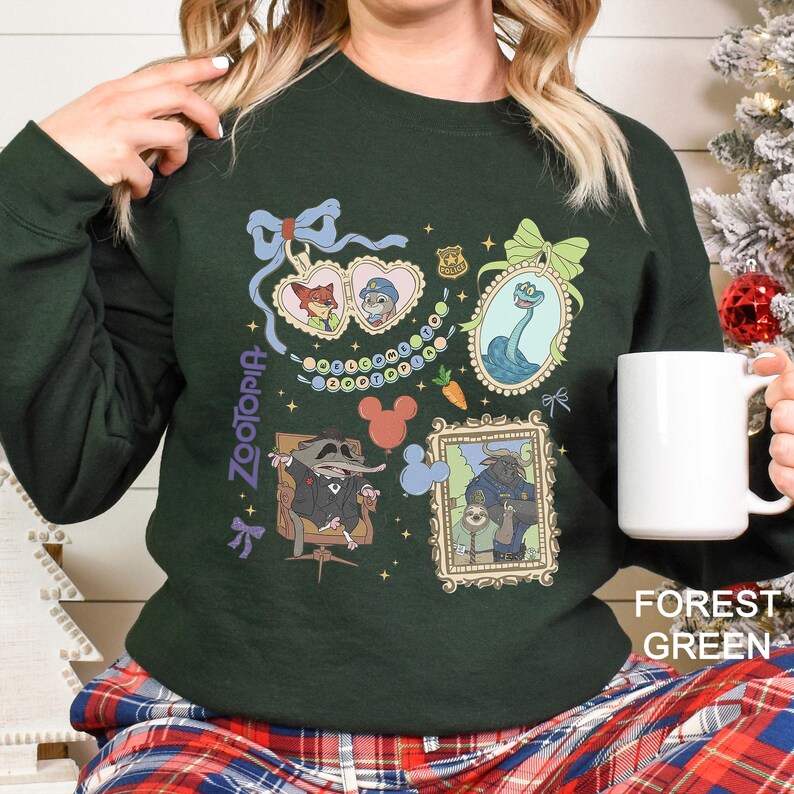 以下が含まれることがあります： ズートピアのキャラクターの額入りイラストが特徴のフォレストグリーンのスウェットシャツ。デザインには、ニック・ワイルドとジュディ・ホップス、ヘビ、その他のキャラクターが含まれています。「ズートピア」の文字がスウェットシャツの左側に縦にプリントされています。