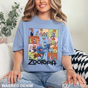 May include: A light blue t-shirt featuring a colorful graphic from the movie Zootopia. The graphic includes various characters from the film, with the word "Zootopia" in large black letters. The shirt is made of a soft material and is a washed denim color.
