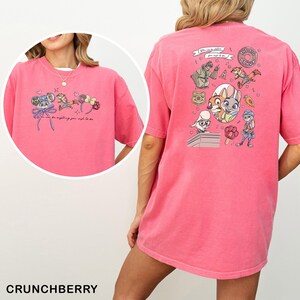 May include: A pink t-shirt with cartoon characters and the text "You can be anything you wish to be." The back of the shirt has cartoon graphics and the words "The Big Donut."