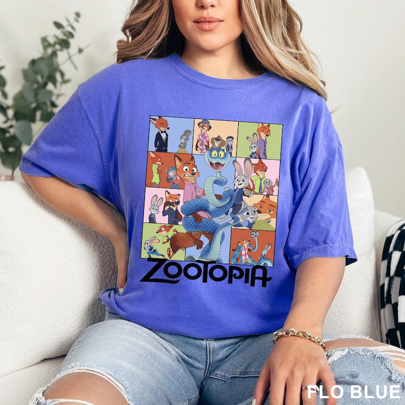 May include: A blue t-shirt with a colourful graphic from the animated film "Zootopia." The design features characters from the film in a grid, with the word "Zootopia" in black at the bottom. The shirt is labelled "FLO BLUE" at the bottom right.