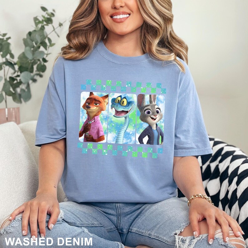 May include: A light blue t-shirt featuring three cartoon characters: a fox in a pink shirt, a snake, and a rabbit in a blue jacket. The shirt has the words "WASHED DENIM" at the bottom.