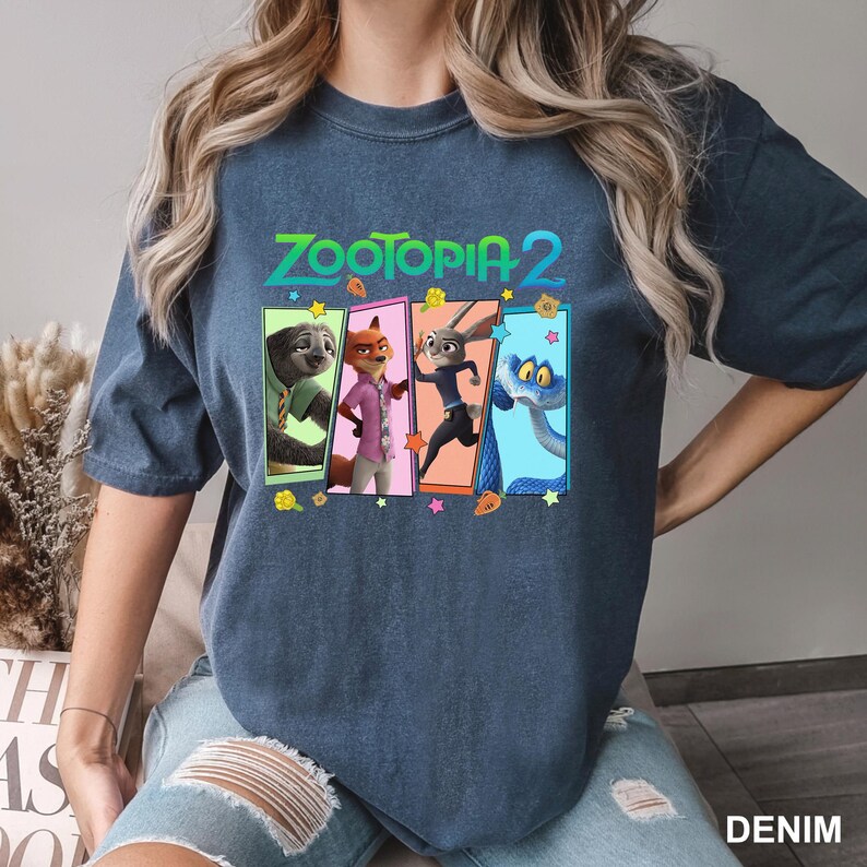 May include: A denim blue t-shirt featuring the text "ZOOTOPIA 2" above a colorful graphic of characters from the animated movie. The graphic includes a sloth, fox, rabbit, and snake. The word "DENIM" is printed at the bottom right.