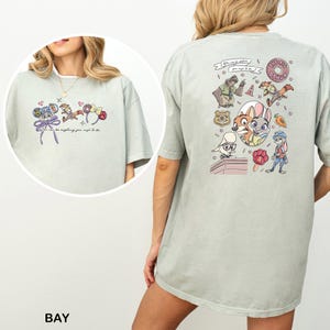 May include: Pale green t-shirt with cartoon characters and the text "You can be anything you wish to be." The back of the shirt has a colourful graphic with more cartoon characters and the words "THE BIG DONUT."