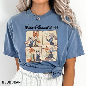 K&ouml;nnte beinhalten: Blaues Jeans-T-Shirt mit einer Grafik von Charakteren aus Zootopia. Das Design umfasst vier Panels mit Nick Wilde und Judy Hopps in verschiedenen Posen, mit dem Text "Walt Disney World" &uuml;ber den Panels. Das Shirt hat auch den Text "BLUE JEAN" unten.