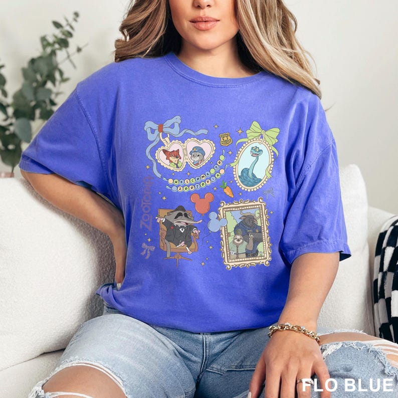 Puede incluir: Una camiseta de manga corta en color azul b&iacute;garo con un estampado gr&aacute;fico de personajes de Zootopia en marcos, incluyendo un relicario en forma de coraz&oacute;n, una serpiente y un perezoso. El dise&ntilde;o incluye estrellas, una zanahoria y el texto Zootopia.