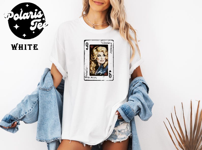 May include: A white short-sleeved t-shirt featuring a graphic print of a playing card with the letter Q and a portrait of a blonde woman. The text Polaris Tee and WHITE are printed in the upper left corner. The shirt is worn with a blue denim jacket.