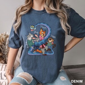 Peut inclure: T-shirt bleu denim avec un dessin anim&eacute; de personnages de film. Le dessin comprend un serpent et plusieurs personnages d'animaux, avec des noms &eacute;crits au-dessus. Le mot "DENIM" est imprim&eacute; en bas &agrave; droite.