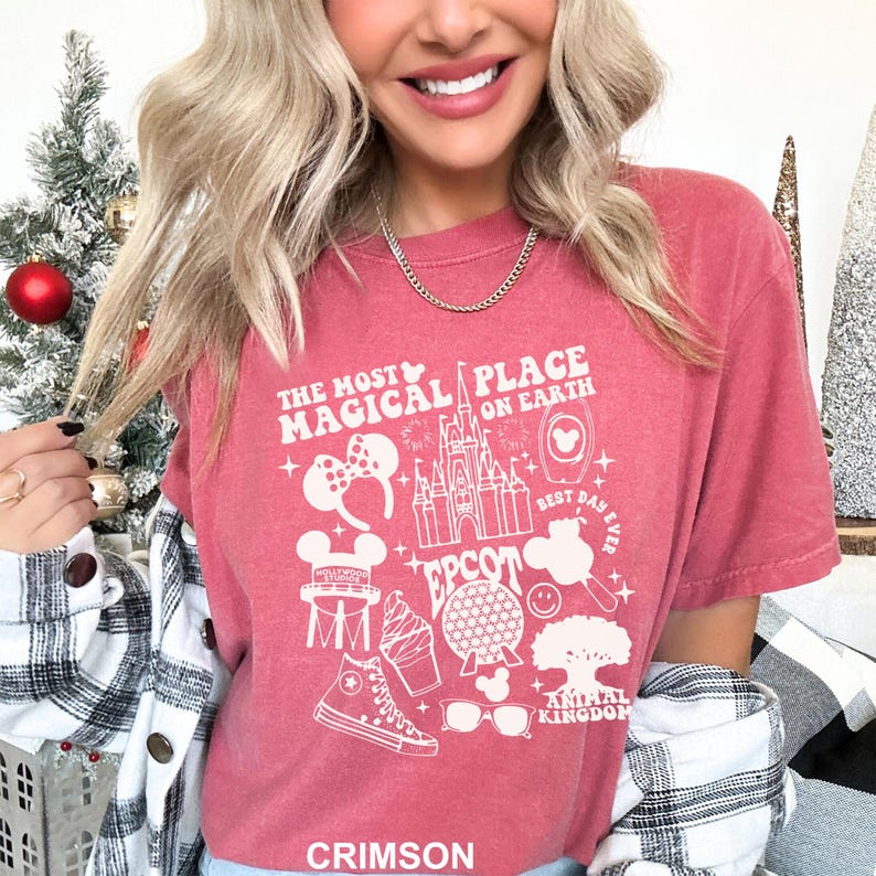 Puede incluir: Camiseta carmes&iacute; con un dise&ntilde;o gr&aacute;fico blanco que presenta el texto "THE MOST MAGICAL PLACE ON EARTH" e iconos tem&aacute;ticos de Disney, como un castillo y orejas de Mickey Mouse.