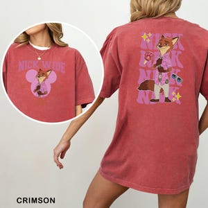 May include: Crimson t-shirt with a cartoon fox character in a pink shirt and sunglasses. The front of the shirt has the text "NICK WIDE" above the fox character. The back of the shirt has the fox character and the text "NICK" repeated.