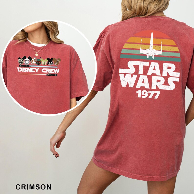 May include: Crimson t-shirt with a "Disney Crew" graphic on the front, showcasing Disney character illustrations. The back features a "Star Wars 1977" design with a retro sunset and a spaceship. The shirt is a comfortable, casual style.