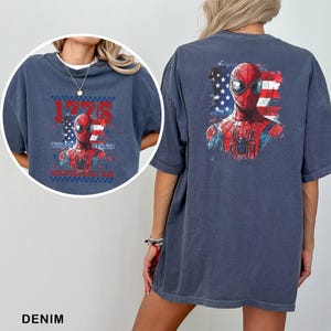 May include: A dark blue t-shirt featuring a graphic of Spider-Man against a distressed American flag background. The front design includes the text 1776 UNITED STATES INDEPENDENCE DAY, while the back displays a larger version of the same character.