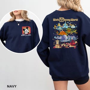 May include: Navy blue sweatshirt featuring Mickey Mouse and the text "Magic Kingdom Since 1971" on the front. The back displays a colorful illustration of Walt Disney World with the words "Walt Disney World".