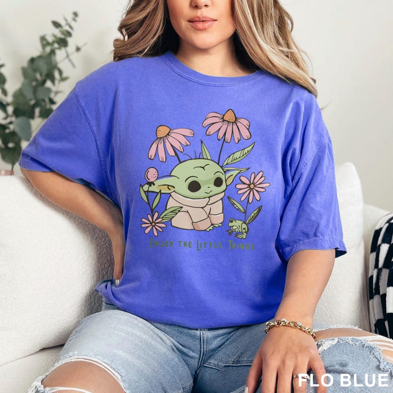 Puede incluir: Camiseta azul con un gr&aacute;fico de un personaje alien&iacute;gena verde rodeado de flores rosas y beige. El texto "Enjoy the little things" est&aacute; impreso debajo. La camiseta es de color azul liso.