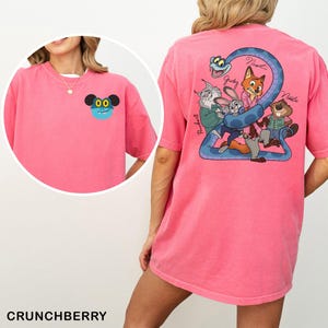 May include: A pink t-shirt featuring a cartoon character on the front and a group of cartoon characters with a blue snake on the back. The text "Crunchberry" is at the bottom of the image.