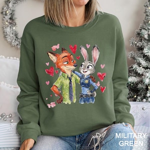 K&ouml;nnte beinhalten: Milit&auml;rgr&uuml;nes Sweatshirt mit einer Aquarellillustration von Nick Wilde und Judy Hopps aus Zootopia, umgeben von rosa Herzen. Nick tr&auml;gt ein gr&uuml;nes Hemd und Krawatte, Judy eine Polizeiuniform.