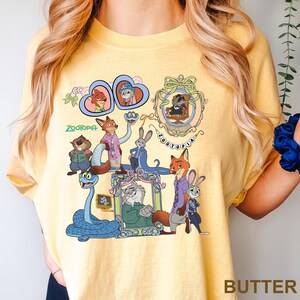 May include: Pale yellow t-shirt with a vibrant graphic of Zootopia characters. The design includes framed portraits and various animal characters, with the word "Zootopia" in green. The shirt is made of a soft material.
