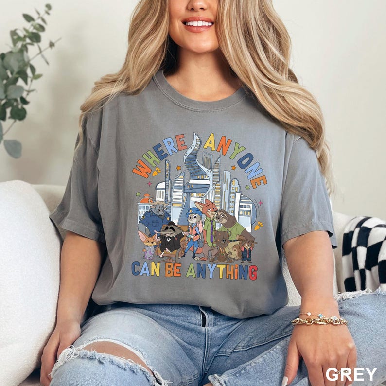 May include: Grey t-shirt with the text "WHERE ANYONE CAN BE ANYTHING" in colorful letters. The shirt features a cartoon illustration of various animal characters in front of a city skyline.