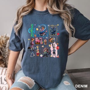May include: A denim-colored short-sleeve t-shirt featuring a multi-panel graphic print of Zootopia characters including Judy Hopps, Nick Wilde, and Flash. The design includes the Zootopia logo, various small icons like a stop sign, and stars.