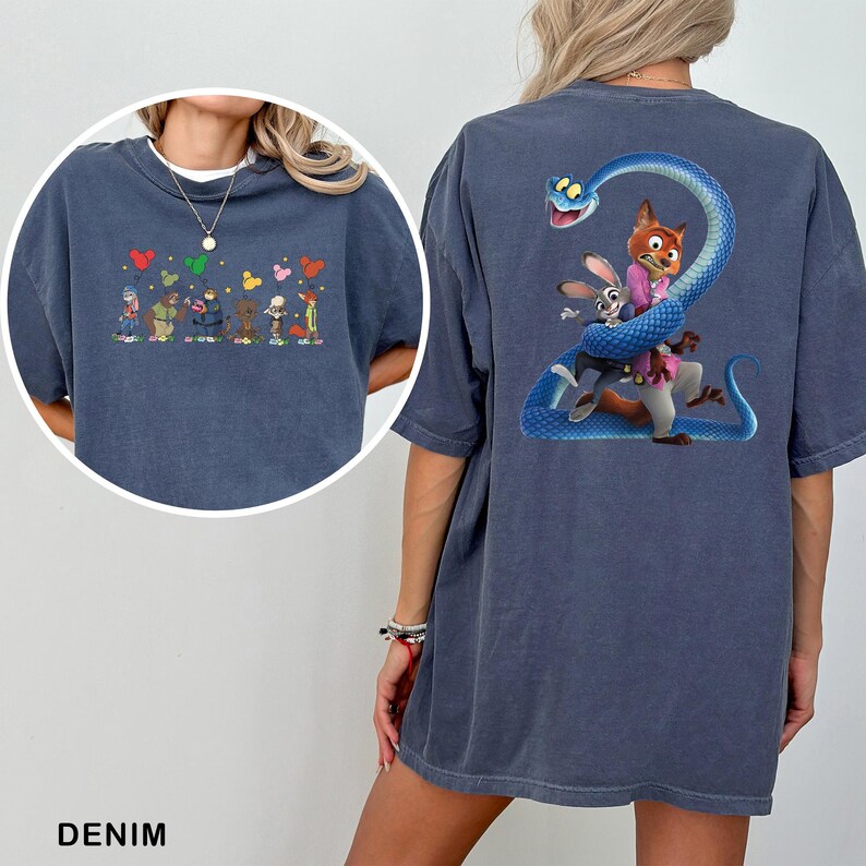 Op de afbeelding: Denim blauw T-shirt met cartoonfiguren op de voor- en achterkant. De voorkant heeft een rij karakters met kleurrijke vormen erboven. De achterkant toont een vos, konijn en slang ontwerp.