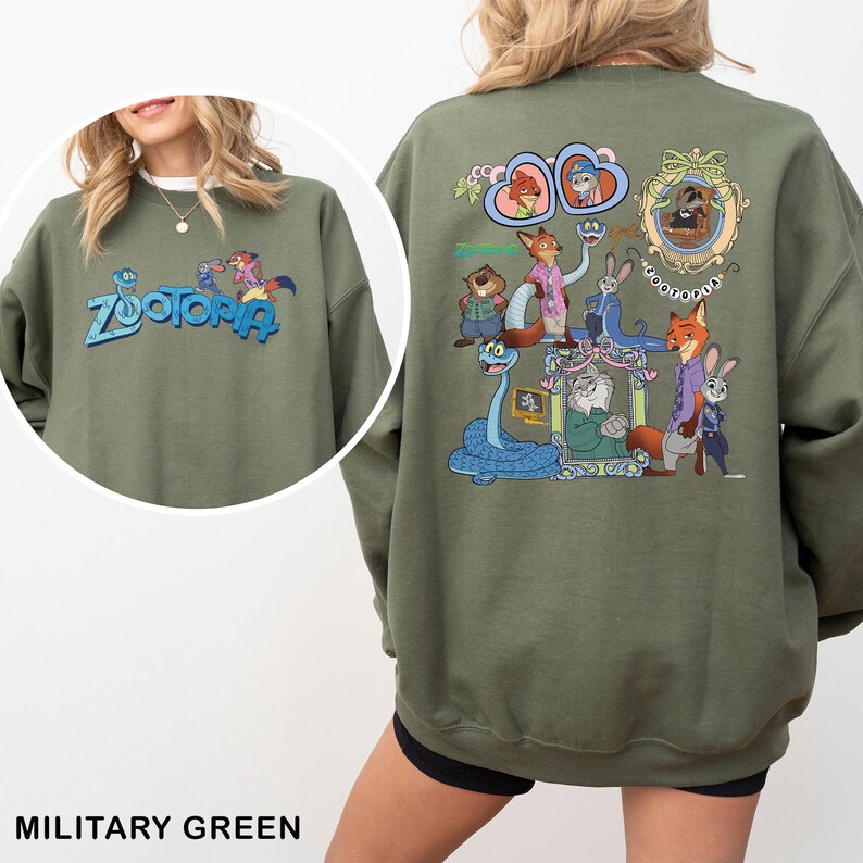 Puede incluir: Sudadera verde militar con la palabra "Zootopia" en azul y un gr&aacute;fico colorido en la parte delantera. La parte trasera muestra una ilustraci&oacute;n detallada de personajes de la pel&iacute;cula animada, incluyendo a Nick Wilde y Judy Hopps.