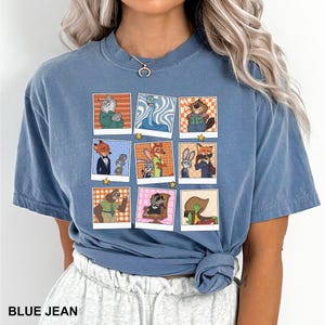 May include: Blue jean colored t-shirt featuring a grid of cartoon character portraits. Each portrait is framed in a white border and includes a star. The shirt has a crew neck and short sleeves. The text "BLUE JEAN" is printed at the bottom.