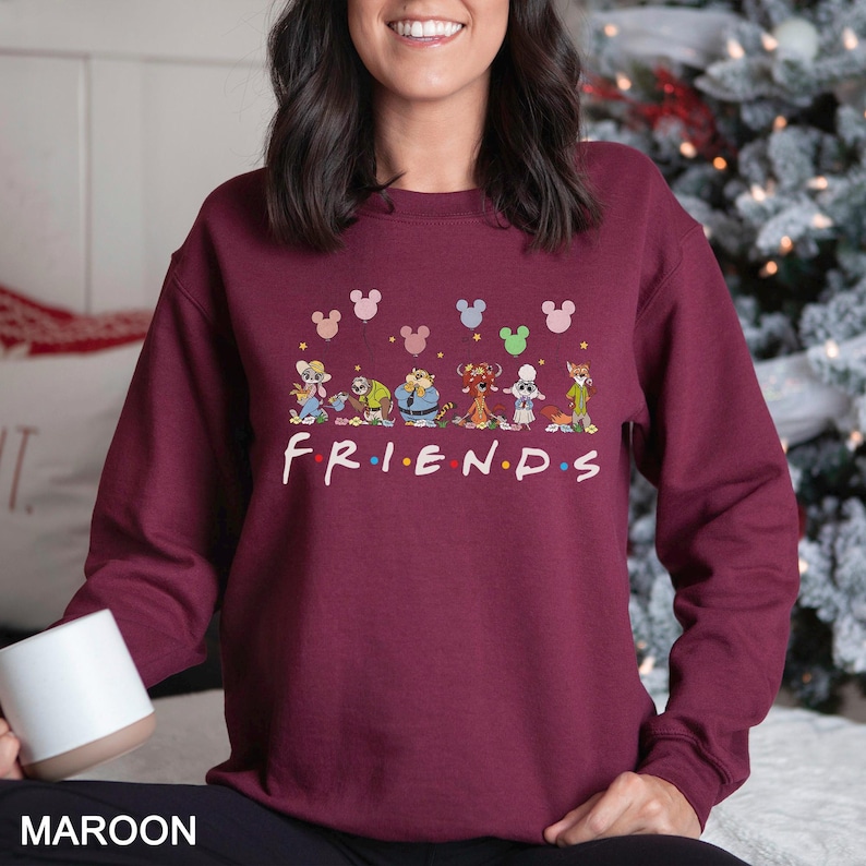 Puede incluir: Sudadera granate con personajes de dibujos animados y la palabra "FRIENDS" en blanco. Encima de la palabra "FRIENDS" hay siluetas de la cabeza de Mickey Mouse en varios colores. La palabra "MAROON" est&aacute; abajo.