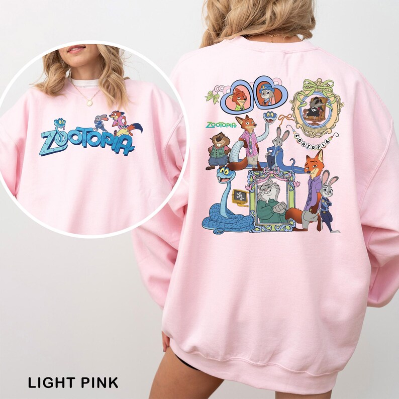 Puede incluir: Sudadera rosa claro con la palabra "Zootopia" en azul y personajes de dibujos animados en la parte delantera y trasera. El dise&ntilde;o trasero incluye im&aacute;genes enmarcadas de personajes y la palabra "Zootopia".