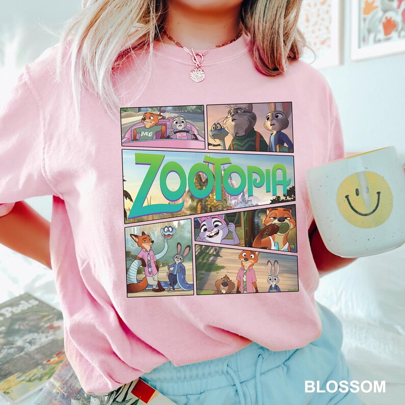 K&ouml;nnte beinhalten: Ein hellrosa T-Shirt mit kurzen &Auml;rmeln und einem Grafikdruck verschiedener Szenen aus dem Film Zootopia, einschlie&szlig;lich des Titels Zootopia in gro&szlig;en gr&uuml;nen Buchstaben. Das Design besteht aus mehreren Feldern mit animierten Figuren.