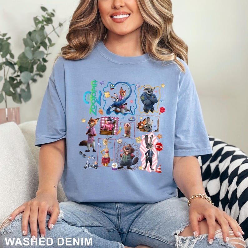 May include: A light blue t-shirt featuring a graphic print of various Zootopia characters including Judy Hopps and Nick Wilde. The design includes the text Zootopia in a vertical orientation, along with several small icons like a stop sign and a scooter.