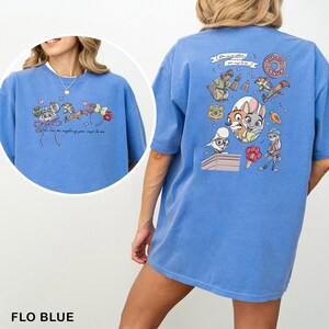 May include: Flo blue t-shirt with cartoon characters and the text "You can be anything you wish to be" on the front. The back of the shirt has a larger graphic with more characters and the words "The Big Donut".