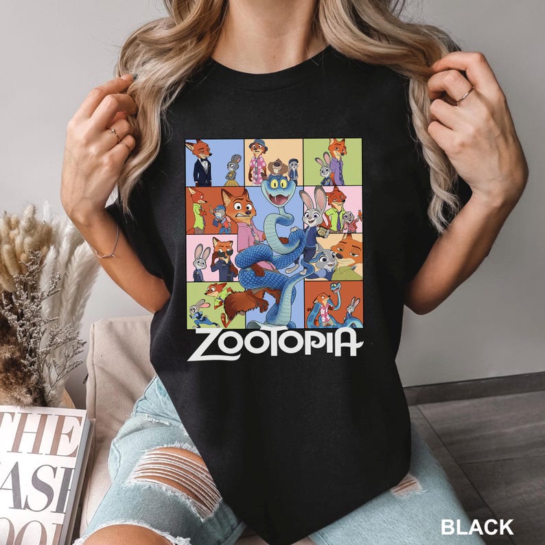May include: Black t-shirt featuring a colorful graphic of characters from the animated movie "Zootopia". The design includes a snake and various animal characters in a grid pattern, with the word "Zootopia" in white text.