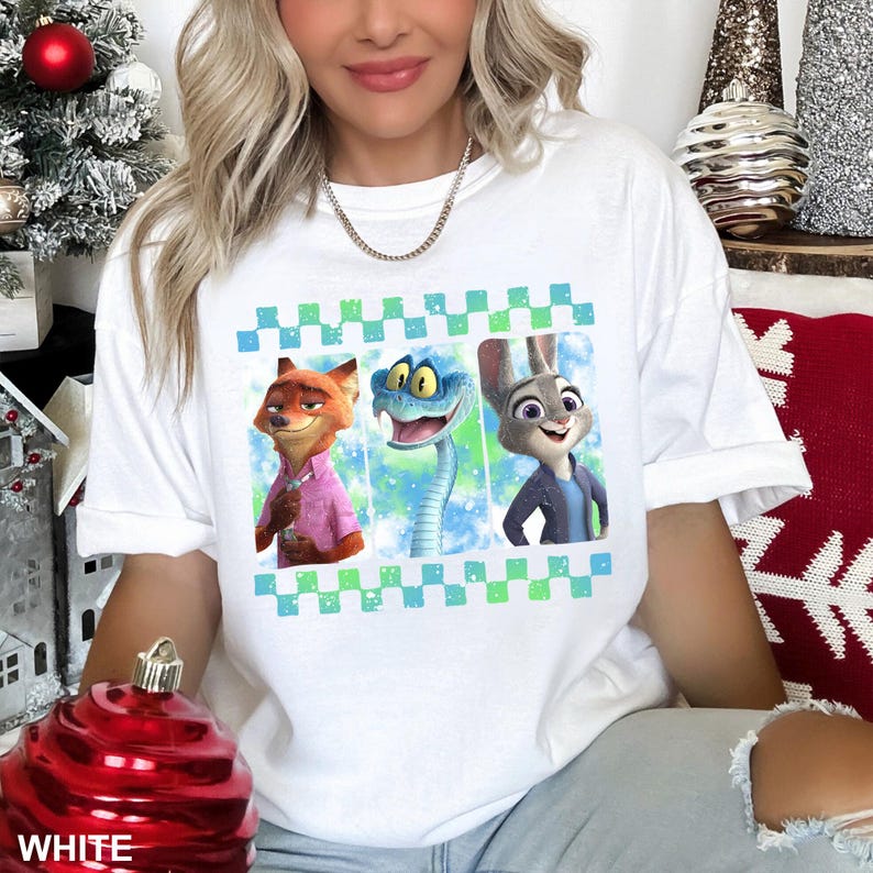May include: White t-shirt featuring a colorful graphic of three cartoon characters: a fox, a snake, and a rabbit. The design is framed by a green and blue checkered pattern. The word "WHITE" is printed at the bottom.
