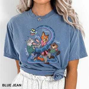 Peut inclure: T-shirt bleu jean avec un motif de dessin anim&eacute; des personnages de Zootopie. Le motif comprend Nick, Judy, Finnick et M. Big, avec le chiffre 2 dans un motif de serpent. Le texte "BLUE JEAN" est en bas.