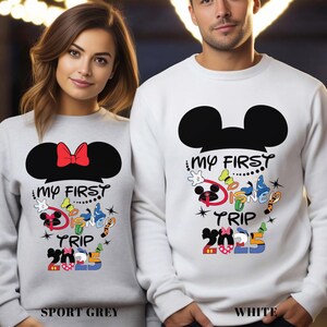 Puede incluir: Sudaderas grises deportivas y blancas con un dise&ntilde;o de orejas de Mickey Mouse y el texto "My First Disney Trip 2025". La sudadera gris deportiva tiene un lazo rojo. La sudadera blanca tiene un dise&ntilde;o de Mickey Mouse.