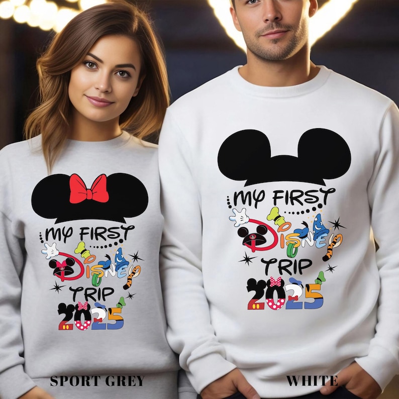 Puede incluir: Sudaderas grises deportivas y blancas con un dise&ntilde;o de orejas de Mickey Mouse y el texto "My First Disney Trip 2025". La sudadera gris deportiva tiene un lazo rojo. La sudadera blanca tiene un dise&ntilde;o de Mickey Mouse.